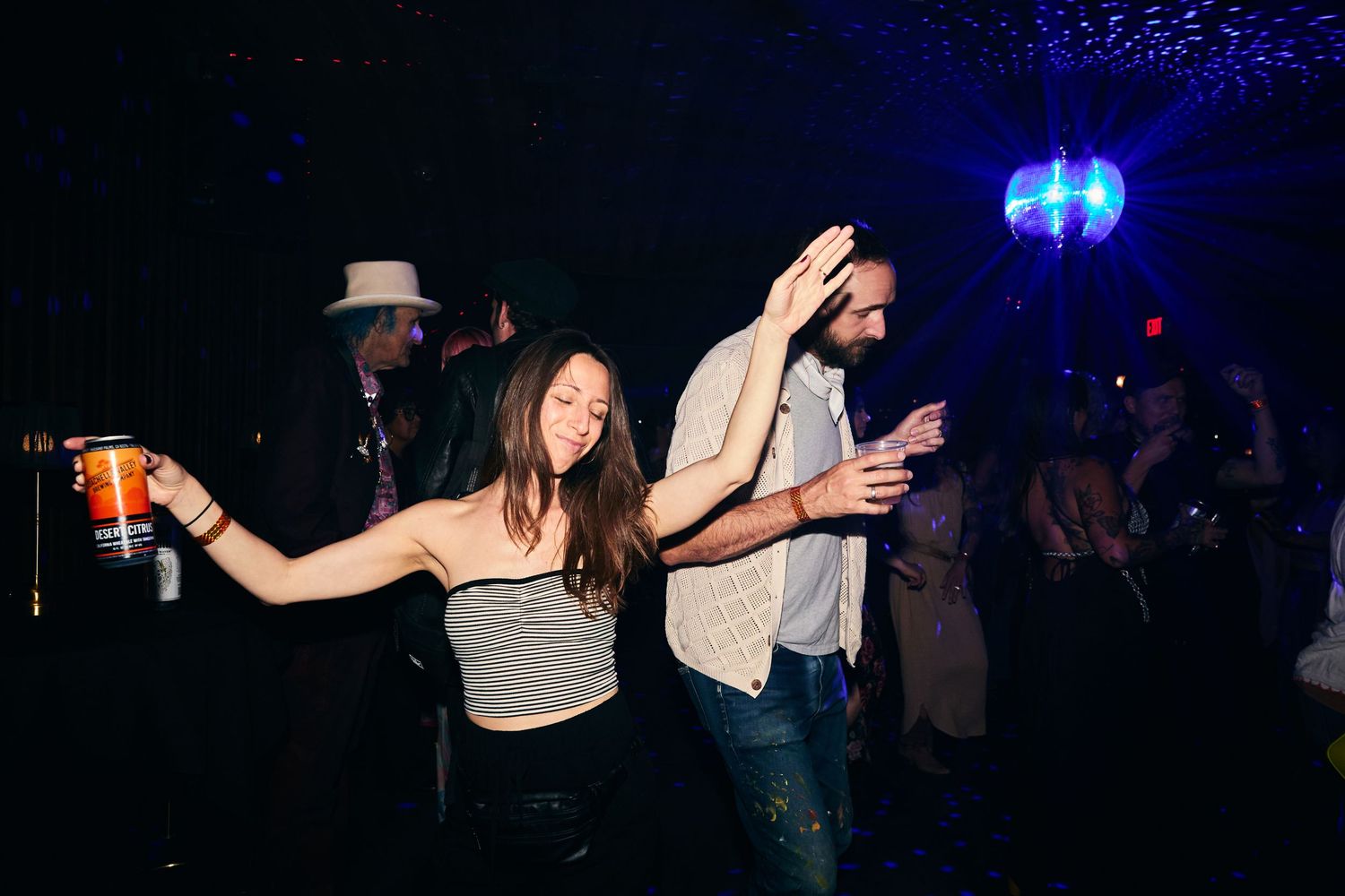 People dancing and having fun at a nightclub with drinks in their hands under dark lighting and a blue disco ball.