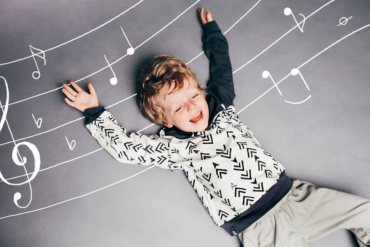 Top-down view of a joyful child in a patterned sweater lying on grey background with illustrated musical notes.