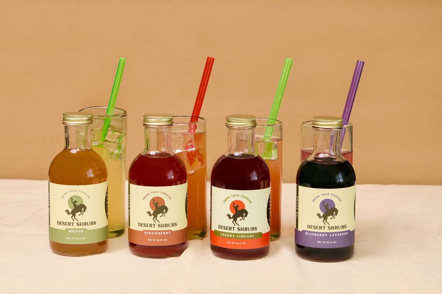 Six colorful bottled beverages with straws in green, red, and purple on a white surface.