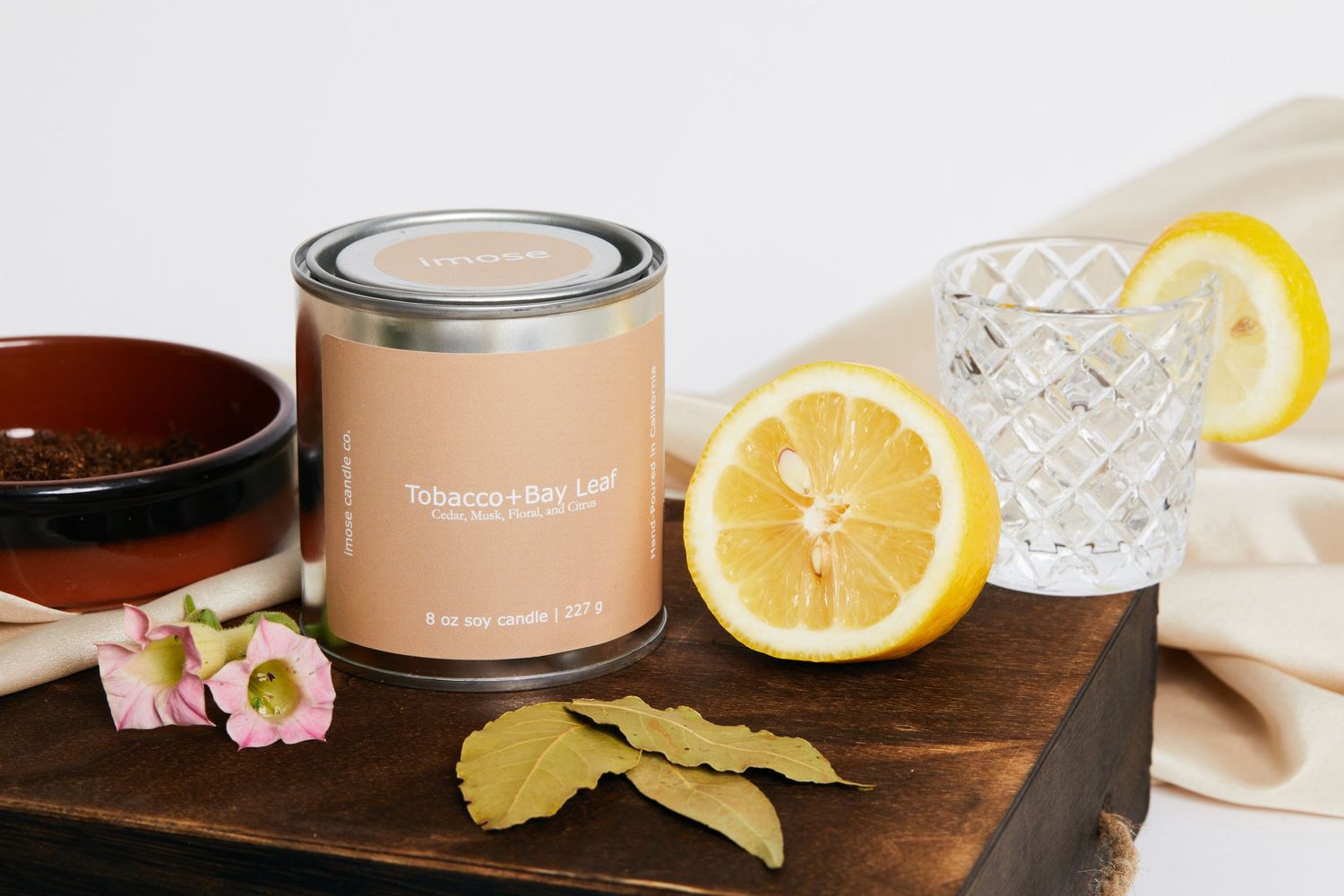 Peachy-colored candle tin displayed with lemon slices and floral accents on wooden surface.
