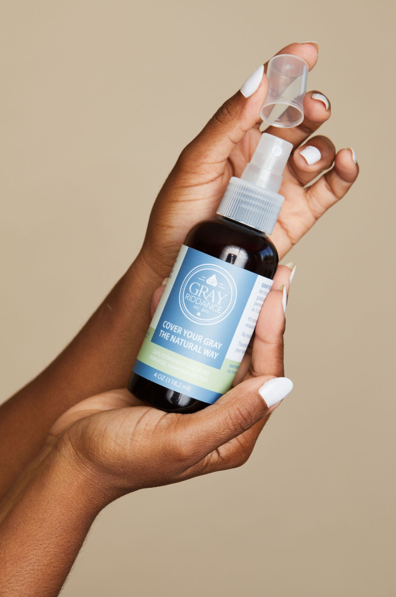 Hands holding blue labeled cosmetic spray bottle against neutral beige background.