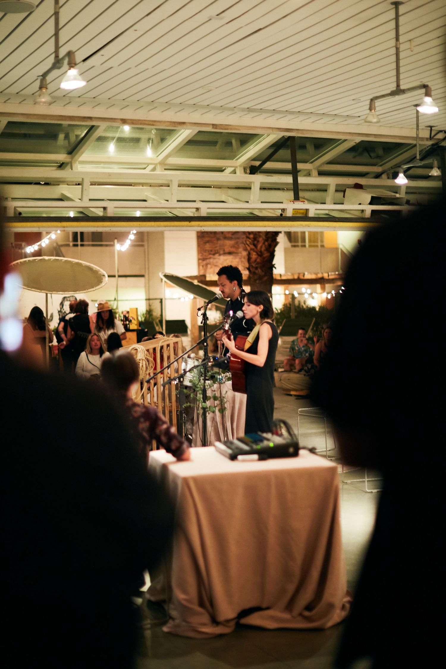 Musicians perform at an intimate indoor venue with draped tables and industrial ceiling during an evening event.