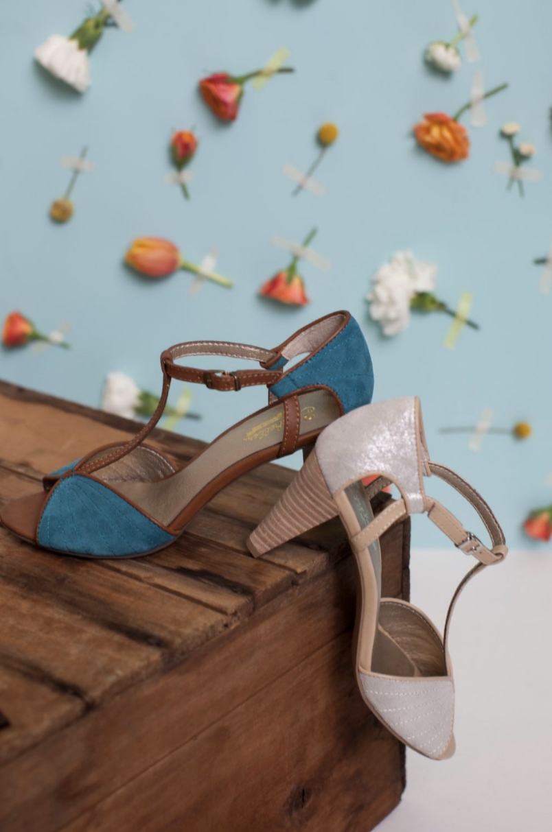 Vintage-style T-strap heels in blue and beige against floral backdrop.