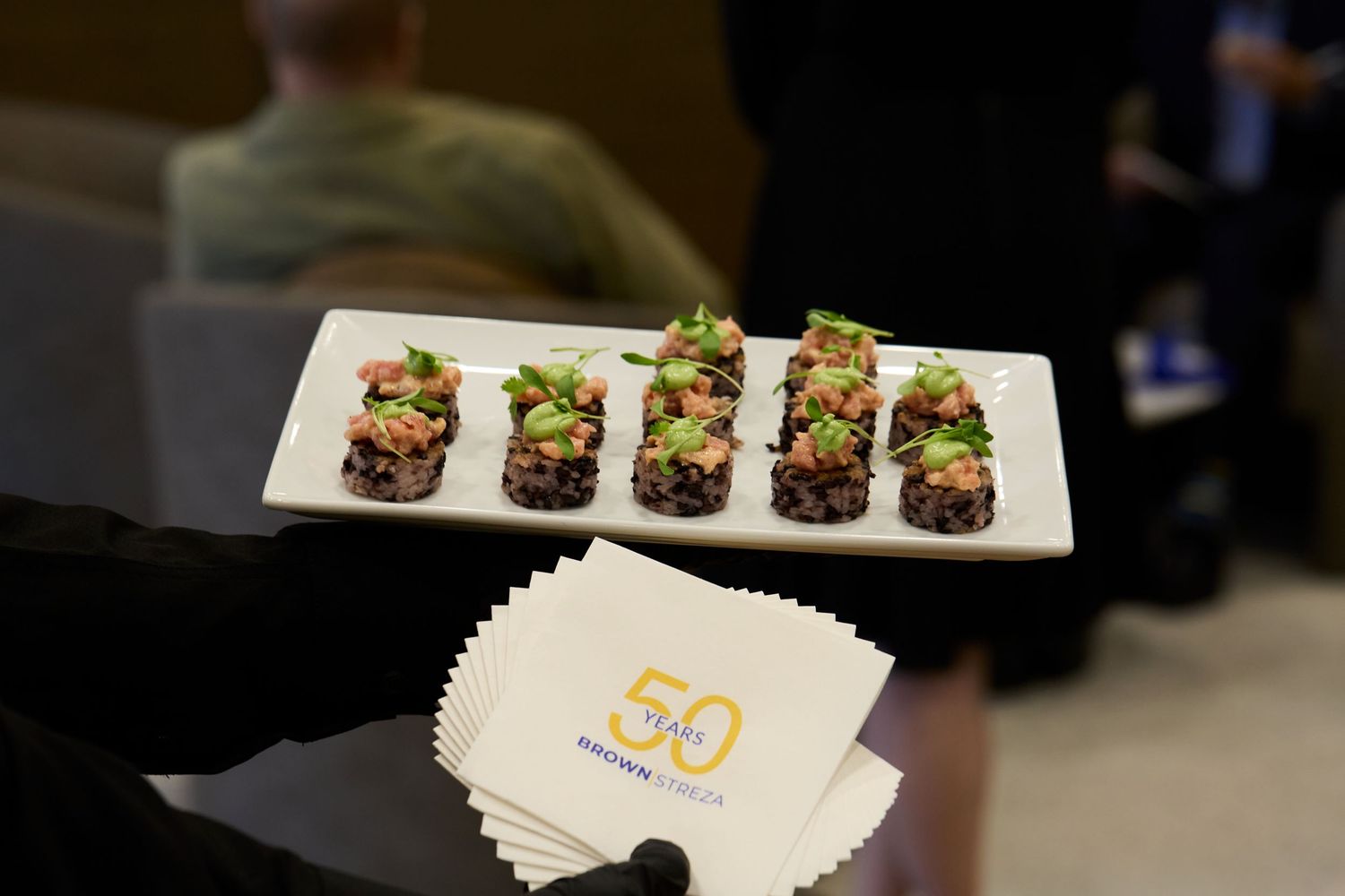 Elegant appetizers served on a white rectangular plate next to branded cocktail napkins at an event.