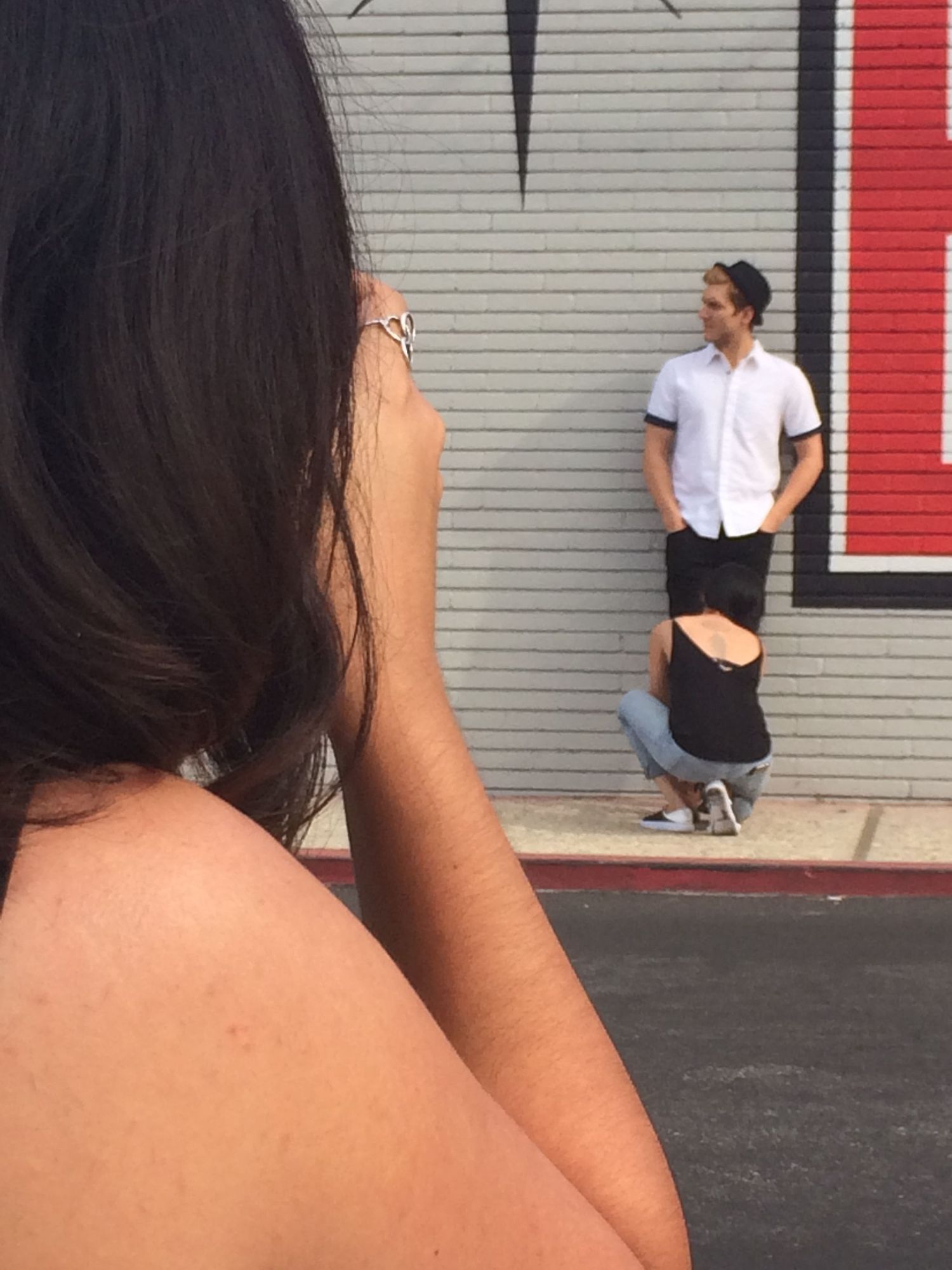 Person in white shirt leans against gray wall with red accent stripe while being photographed from behind shifted perspective.