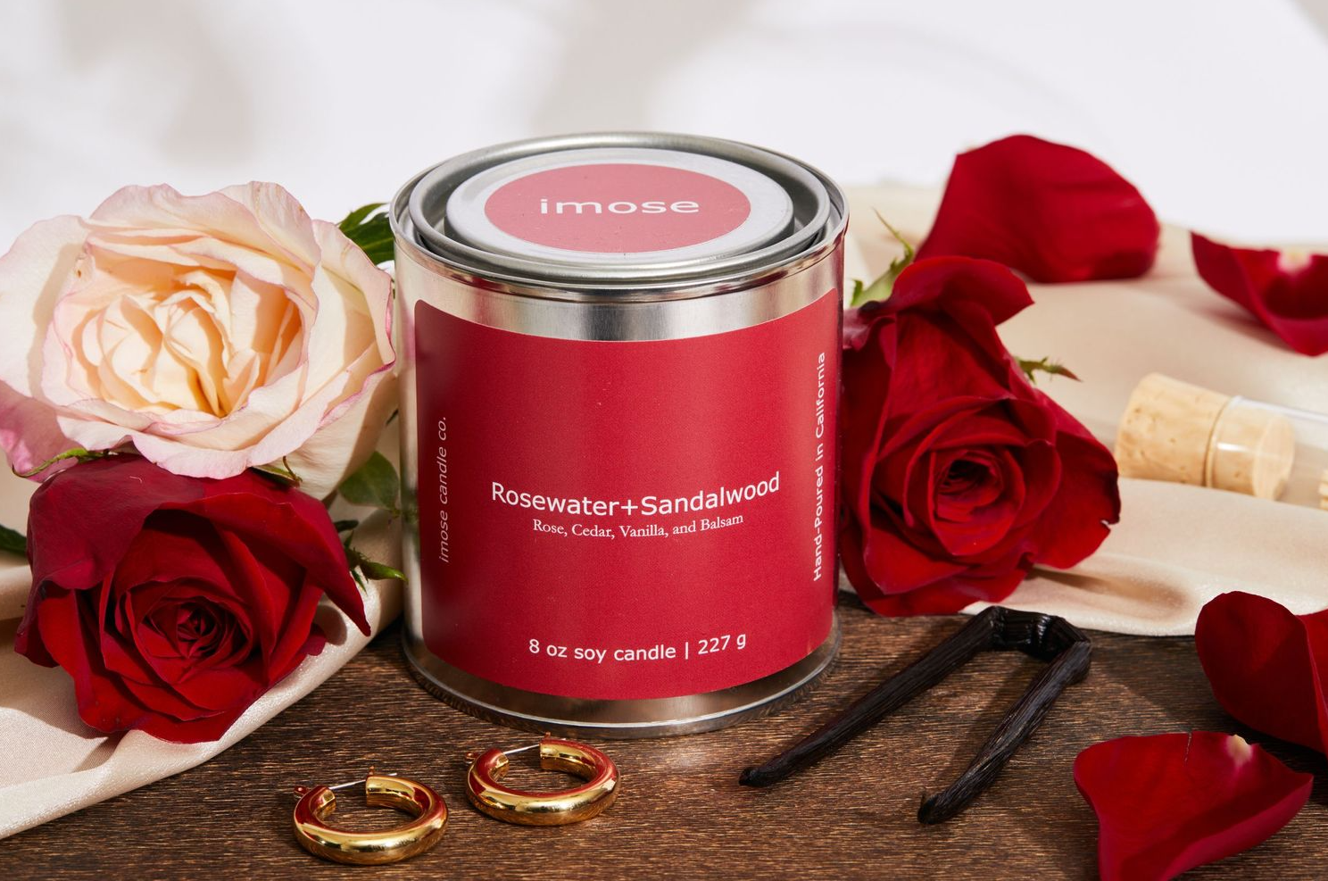 Red candle tin arranged with roses and gold rings in romantic setting.
