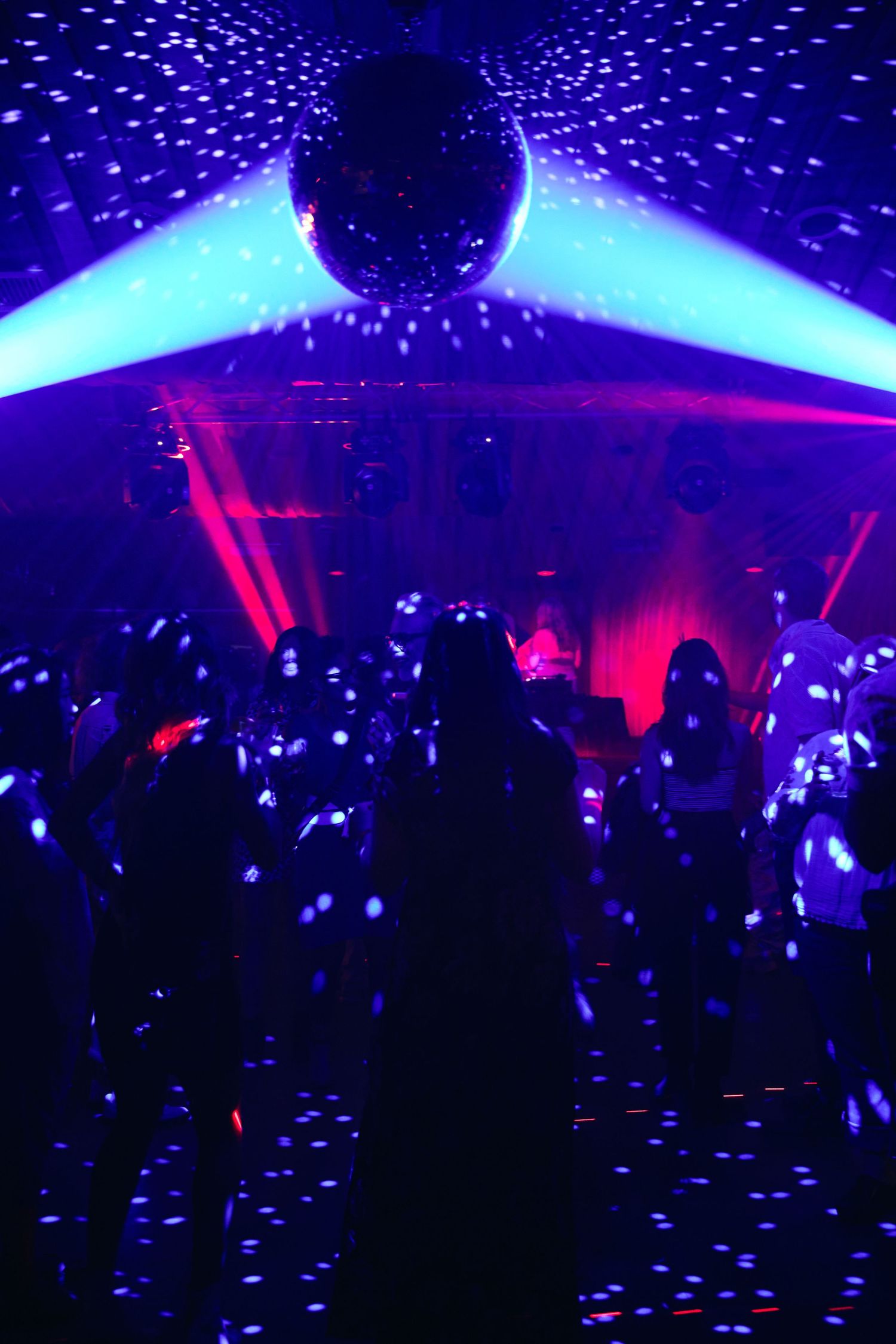 A vibrant nightclub scene with blue and purple lighting effects illuminating a crowded dance floor filled with silhouettes.