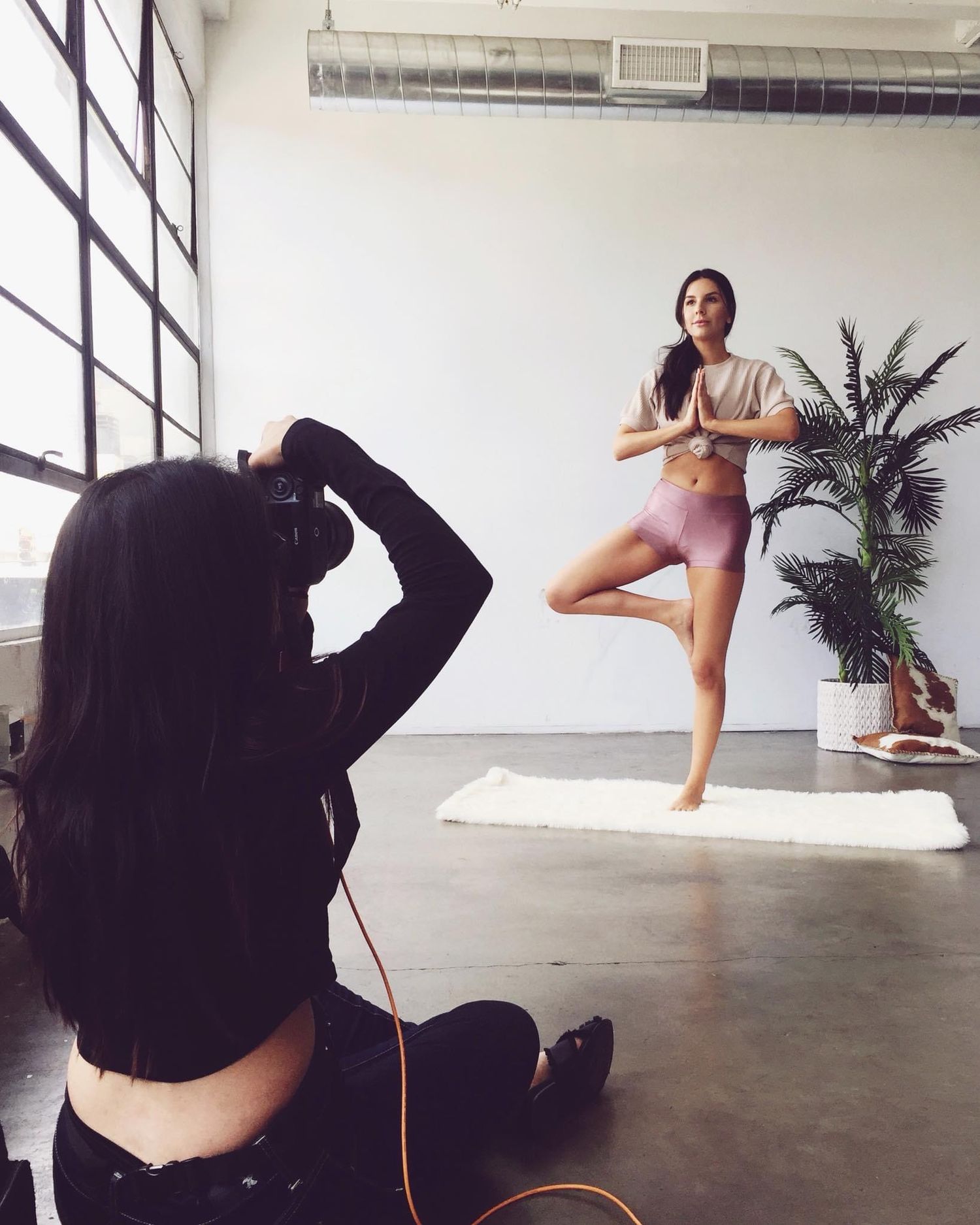 Behind-the-scenes photo of photographer capturing someone in tree pose during a yoga photoshoot in a bright studio space.