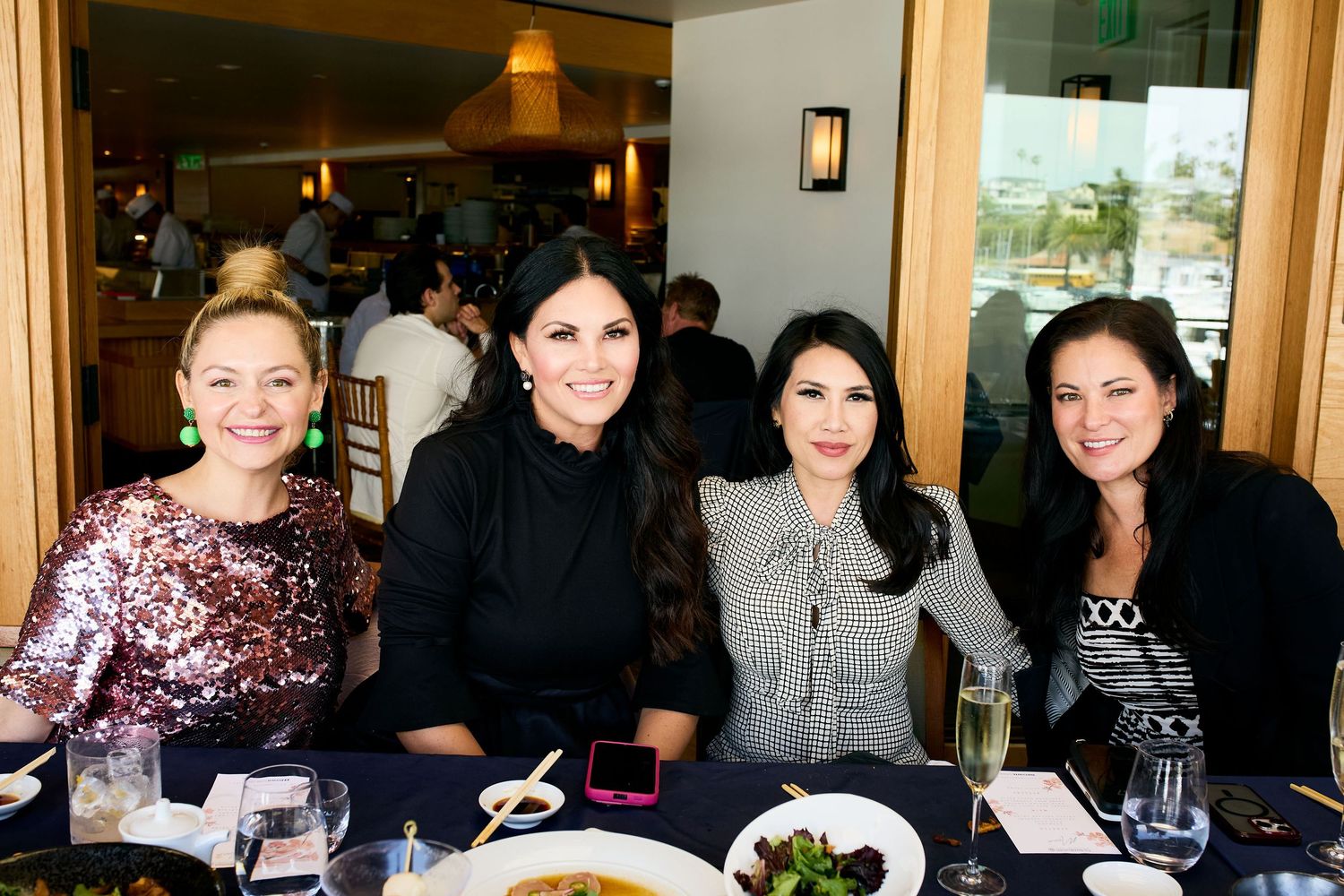 Four women sit together at a restaurant table smiling during a social gathering.