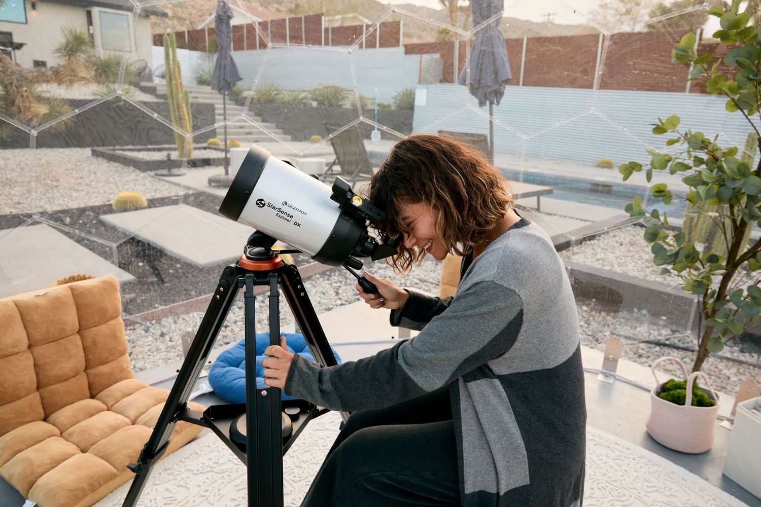 A person sits at a desk with a laptop and camera setup against a backdrop of city buildings and rooftops.