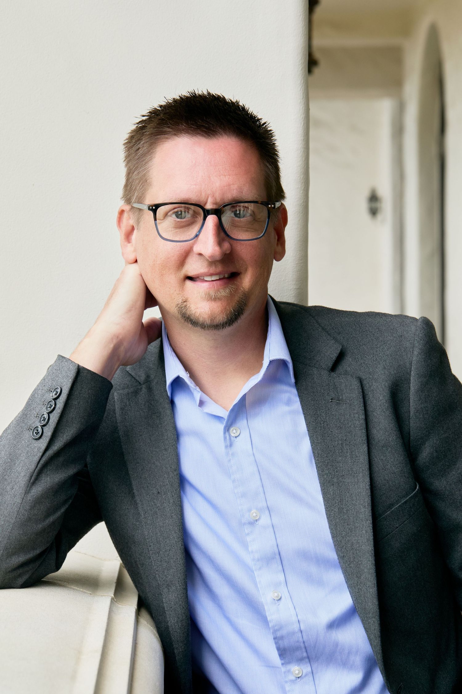 Professional headshot series of a person in business attire against a light background showing different expressions.