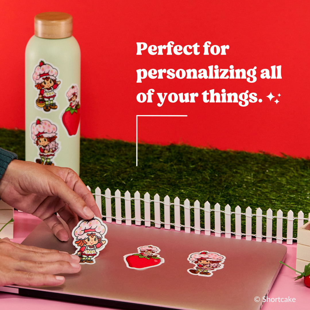 Hands applying Strawberry Shortcake stickers to decorate a light colored water bottle.
