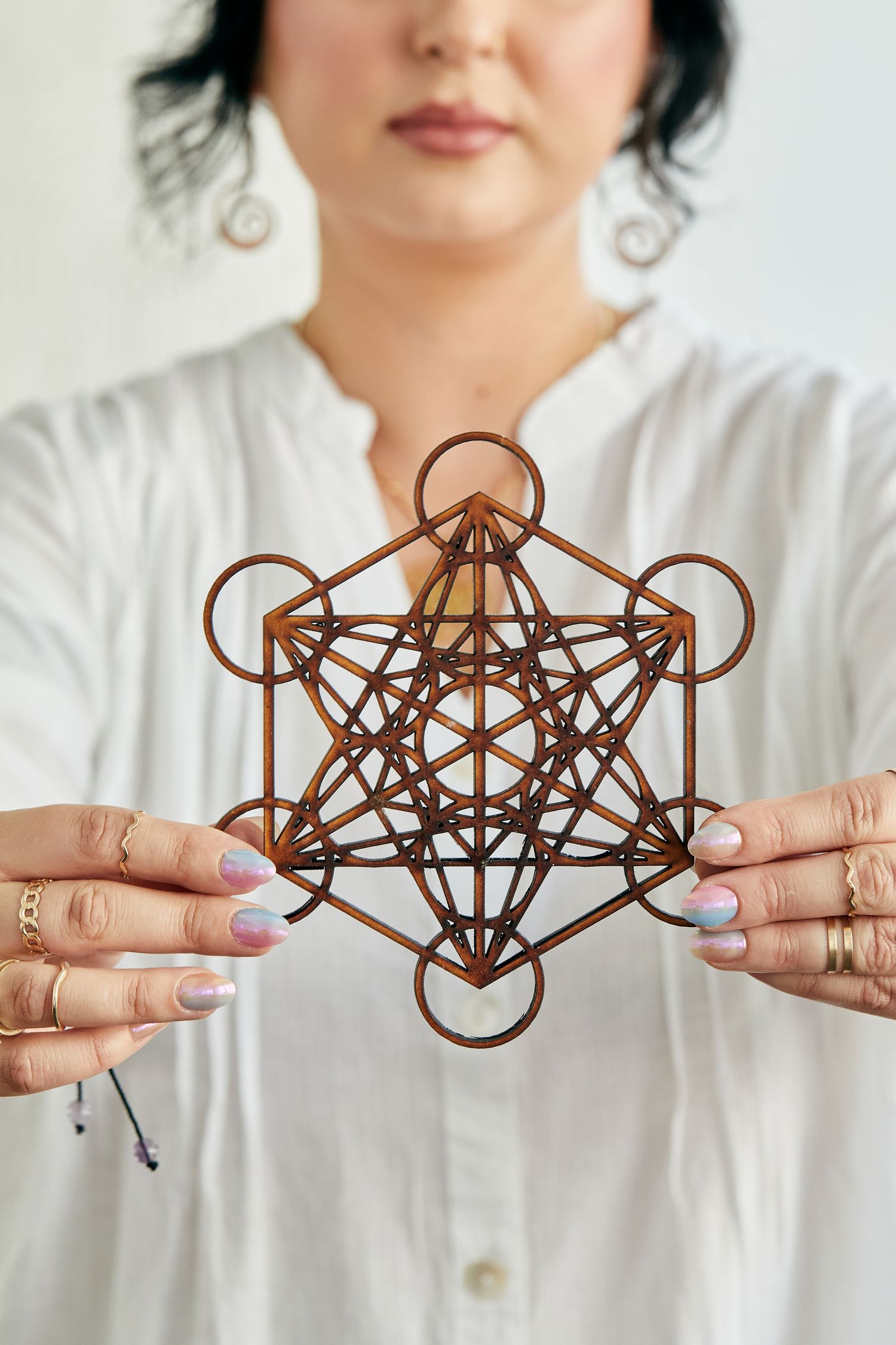 Woman in white holding a wooden Metatrons Cube sacred geometry symbol for spiritual practice.