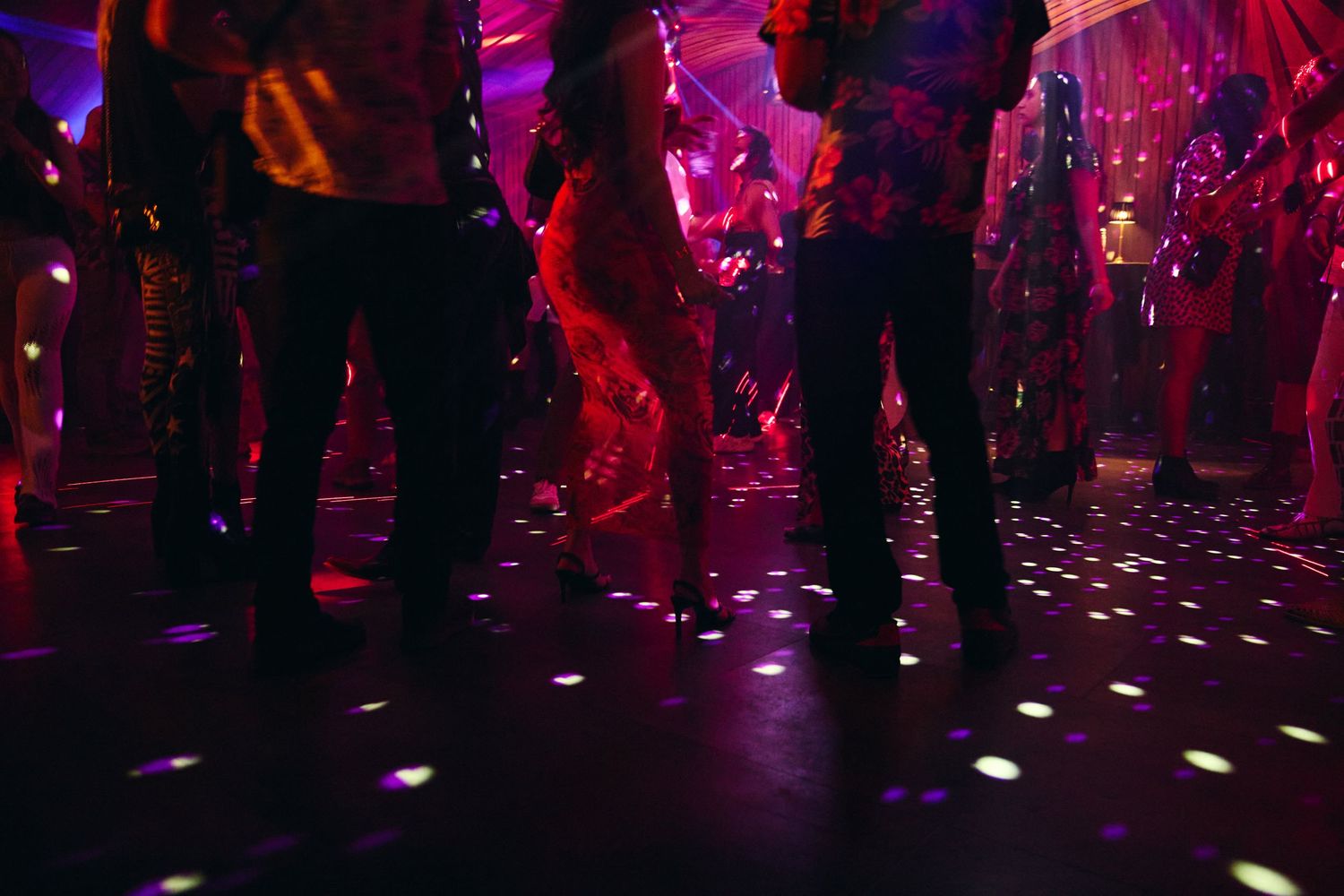 People dance at a nightclub illuminated by vibrant purple lighting and disco effects.