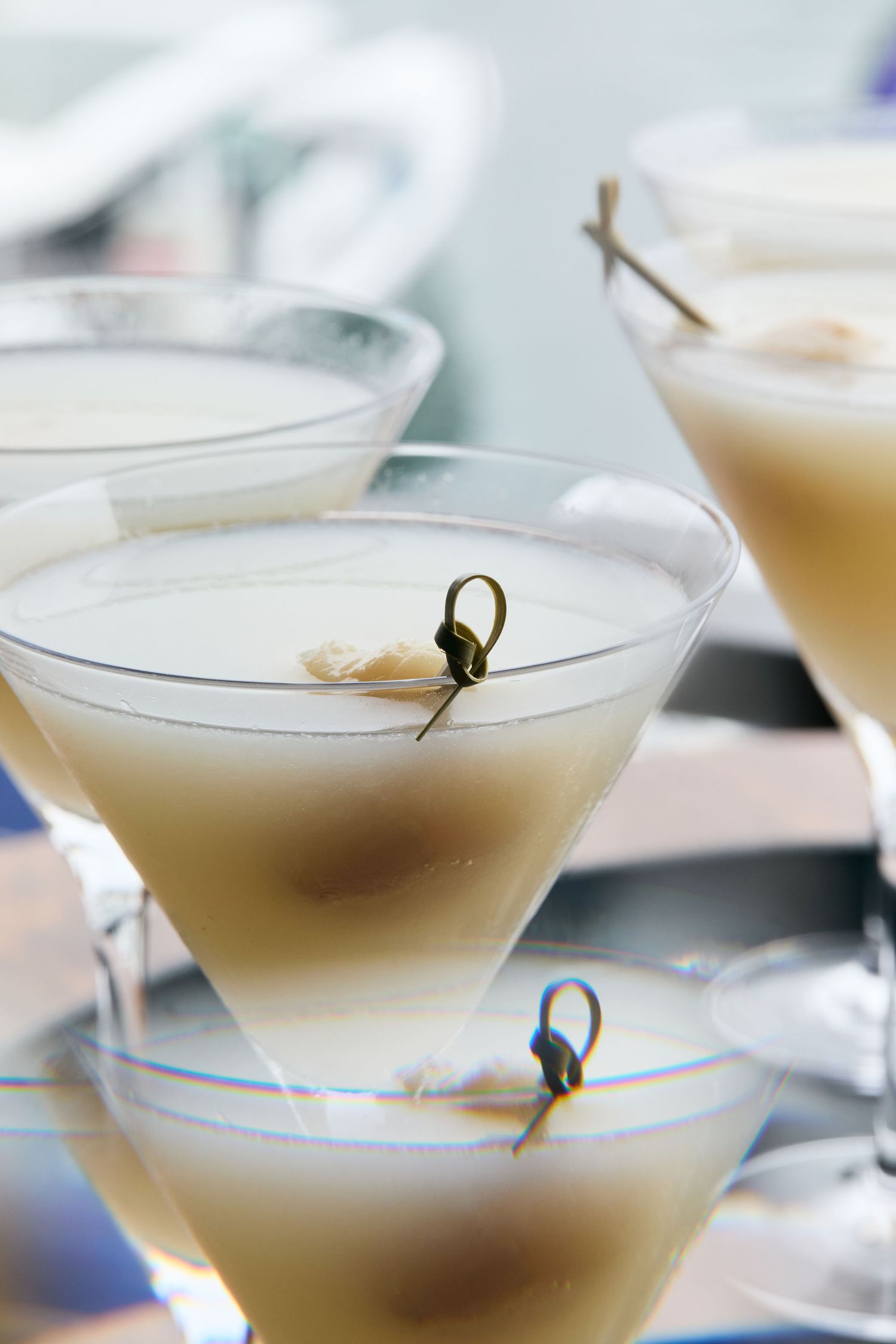 Several martini glasses filled with a creamy beige cocktail and garnished with small skewered olives.