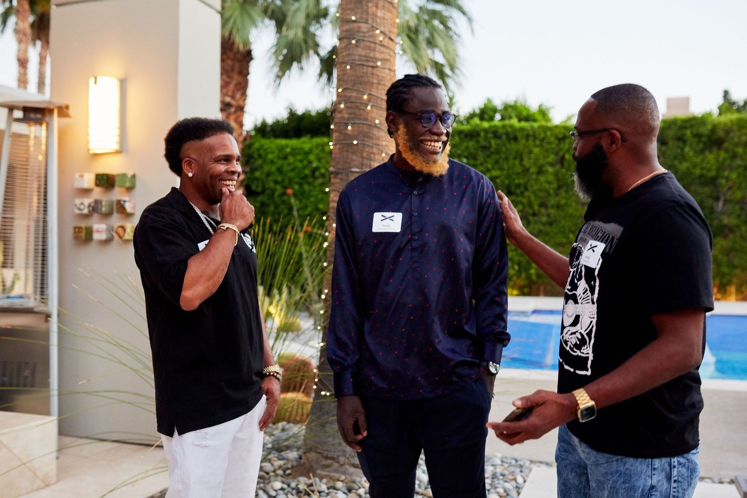 Three friends share a lighthearted moment while socializing outdoors by a pool with palm trees in the background.