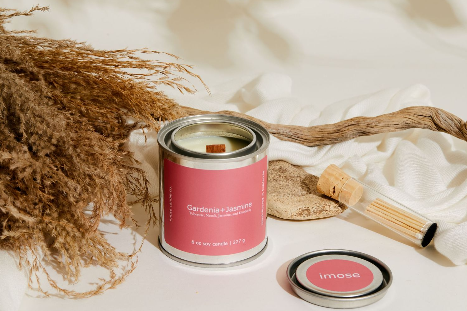 Pink paint can and wood swatch displayed with dried pampas grass against white fabric background.