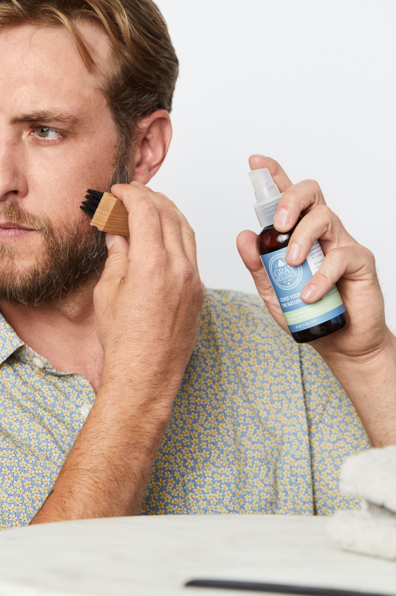 Product demonstration showing application of hair care spray with grooming brush.