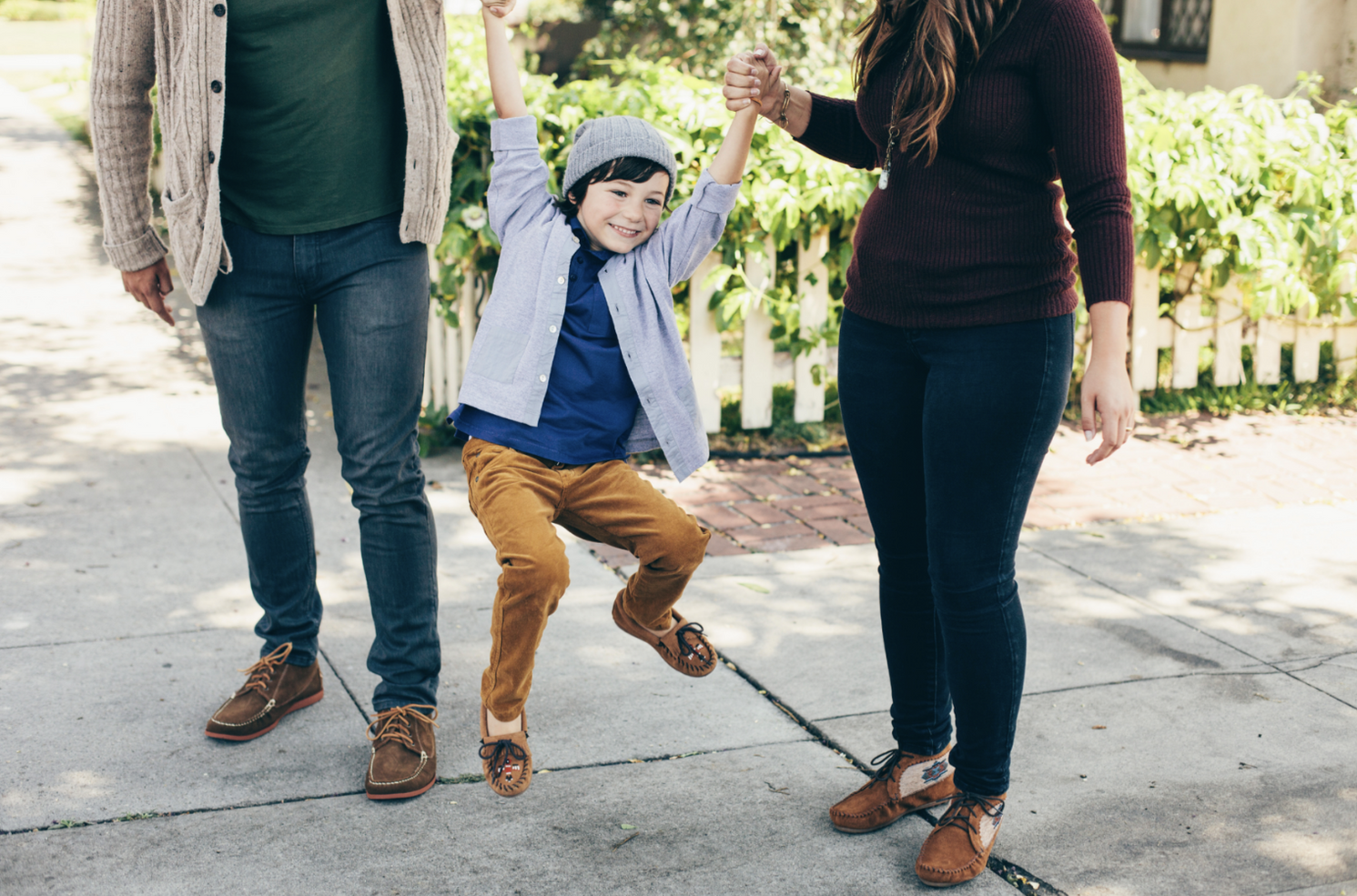 Child jumping playfully between two adults on outdoor walkway.