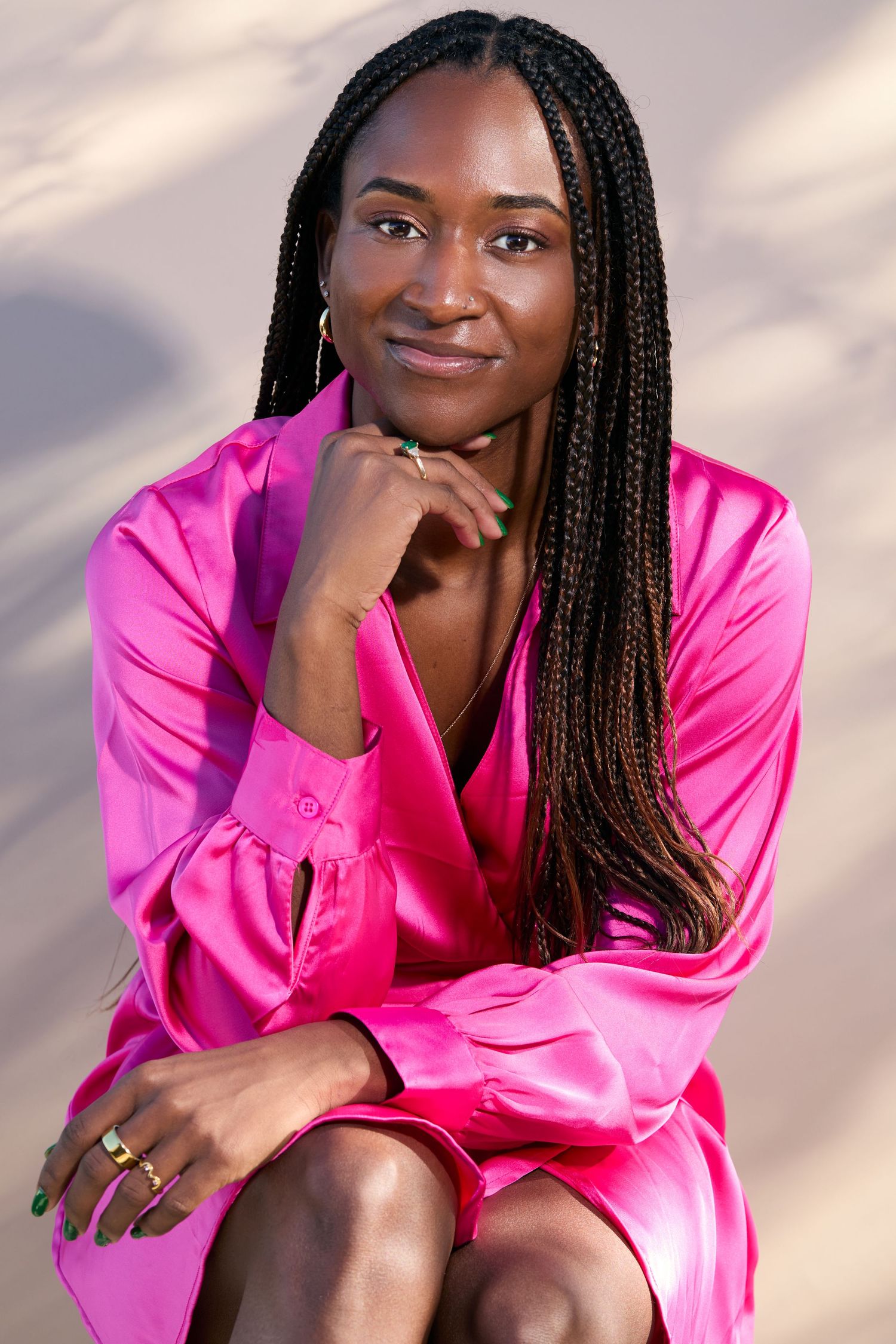 A person in a bright pink satin robe poses against a light background with braided hair and a warm smile.