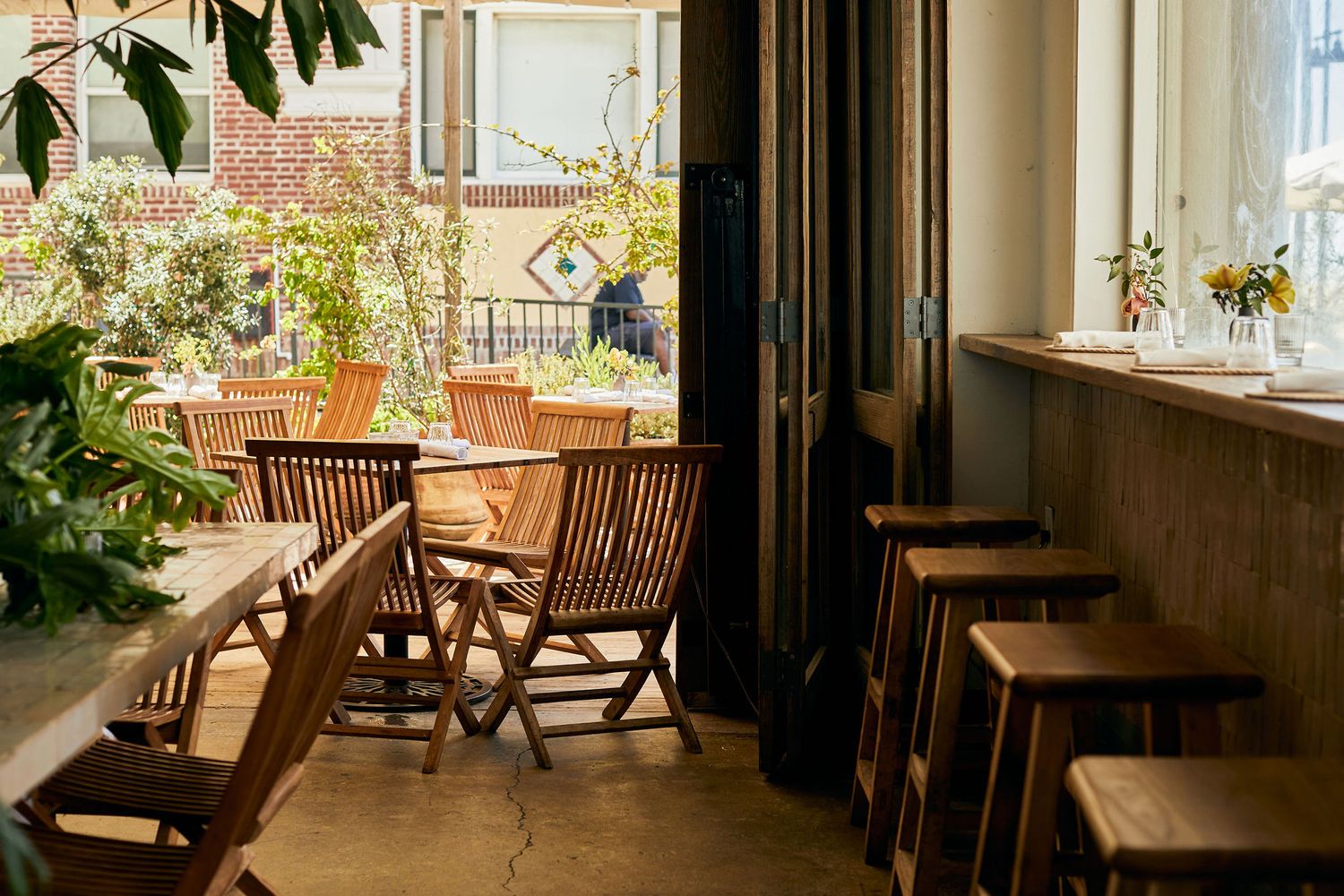 Sunlit cafe terrace with wooden folding chairs and indoor plants.