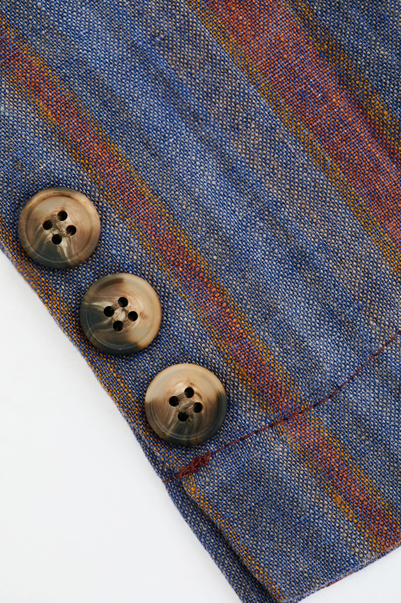 Close-up of blue plaid fabric with three brown buttons on garment edge.