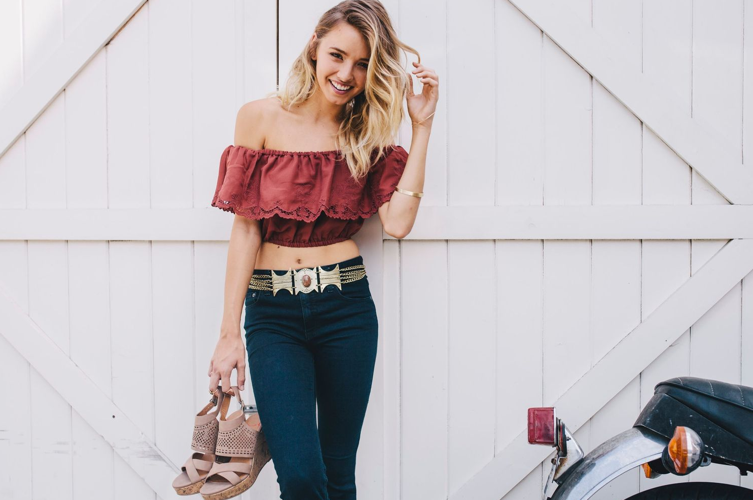 Casual outfit featuring off-shoulder top and jeans photographed against white barn wall.