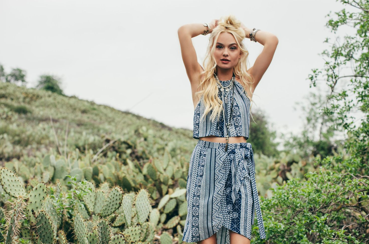 Model in blue patterned dress poses among desert cacti in bohemian photoshoot.