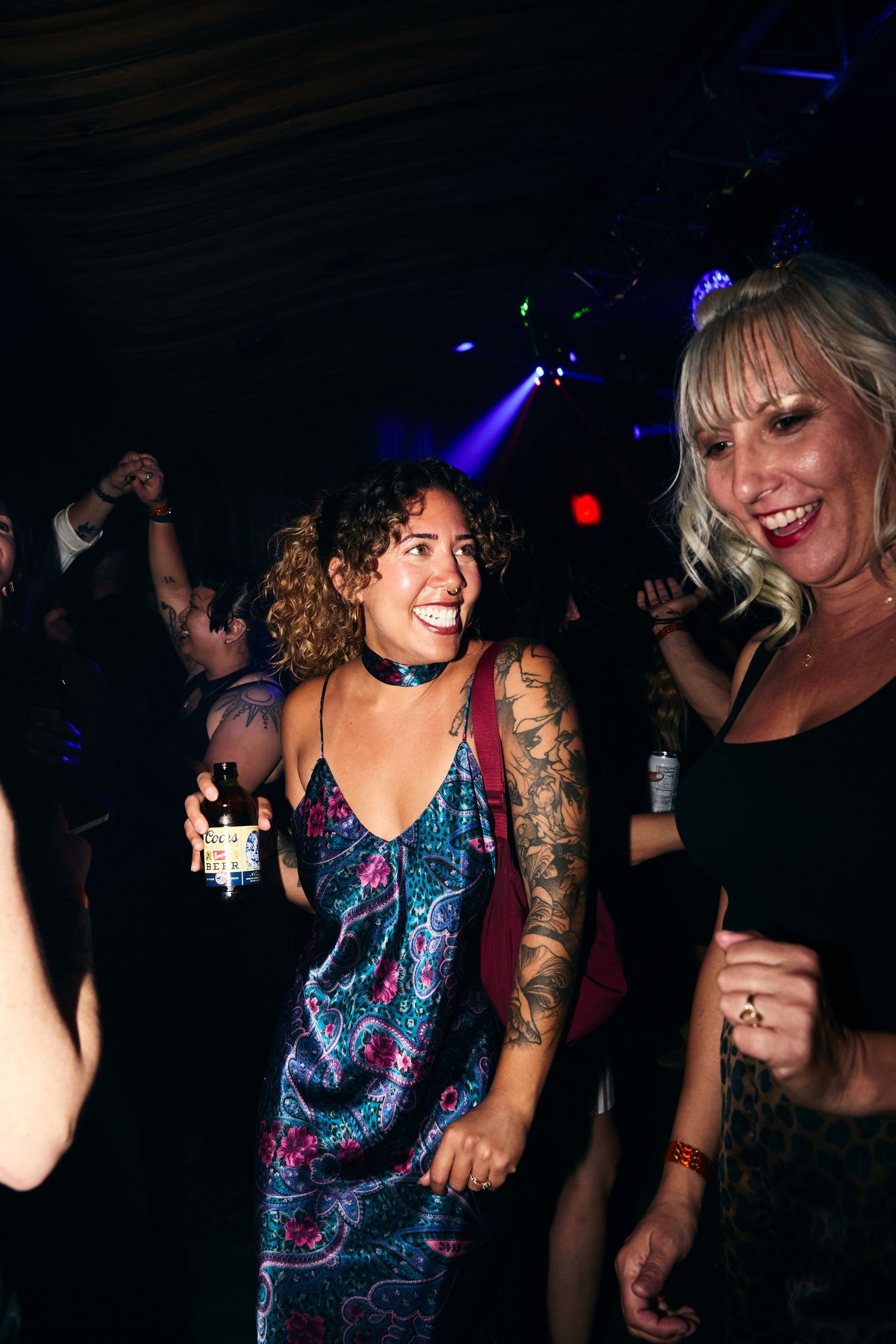 People dancing and having fun at a nightclub with blue lighting and a sparkly dress in view.