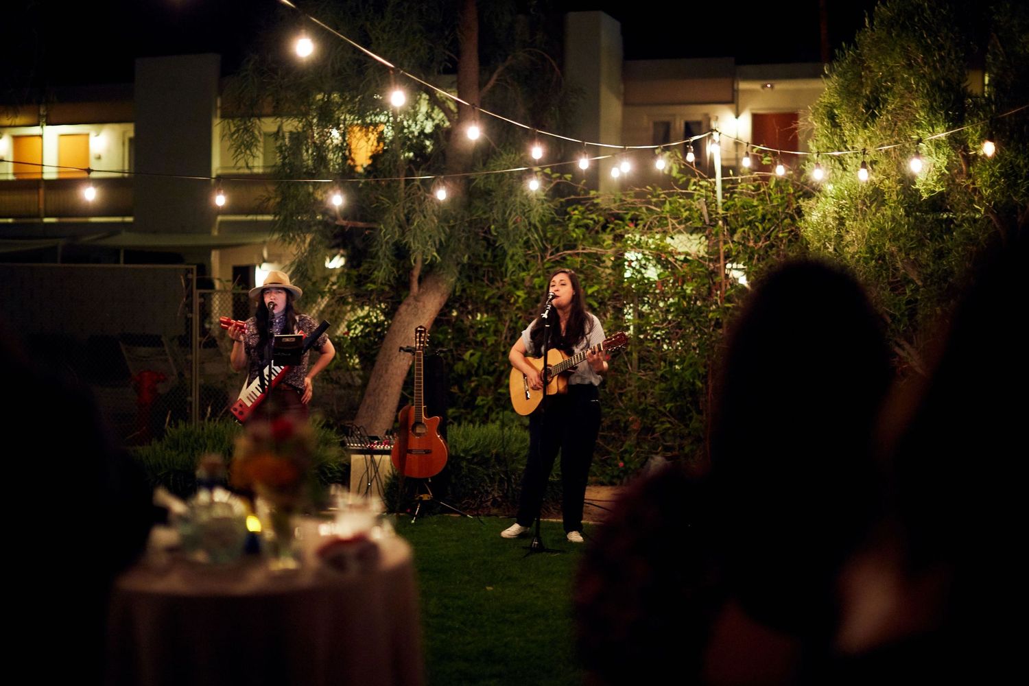 Musicians perform at an intimate outdoor garden party with string lights overhead and cocktail tables in the background.