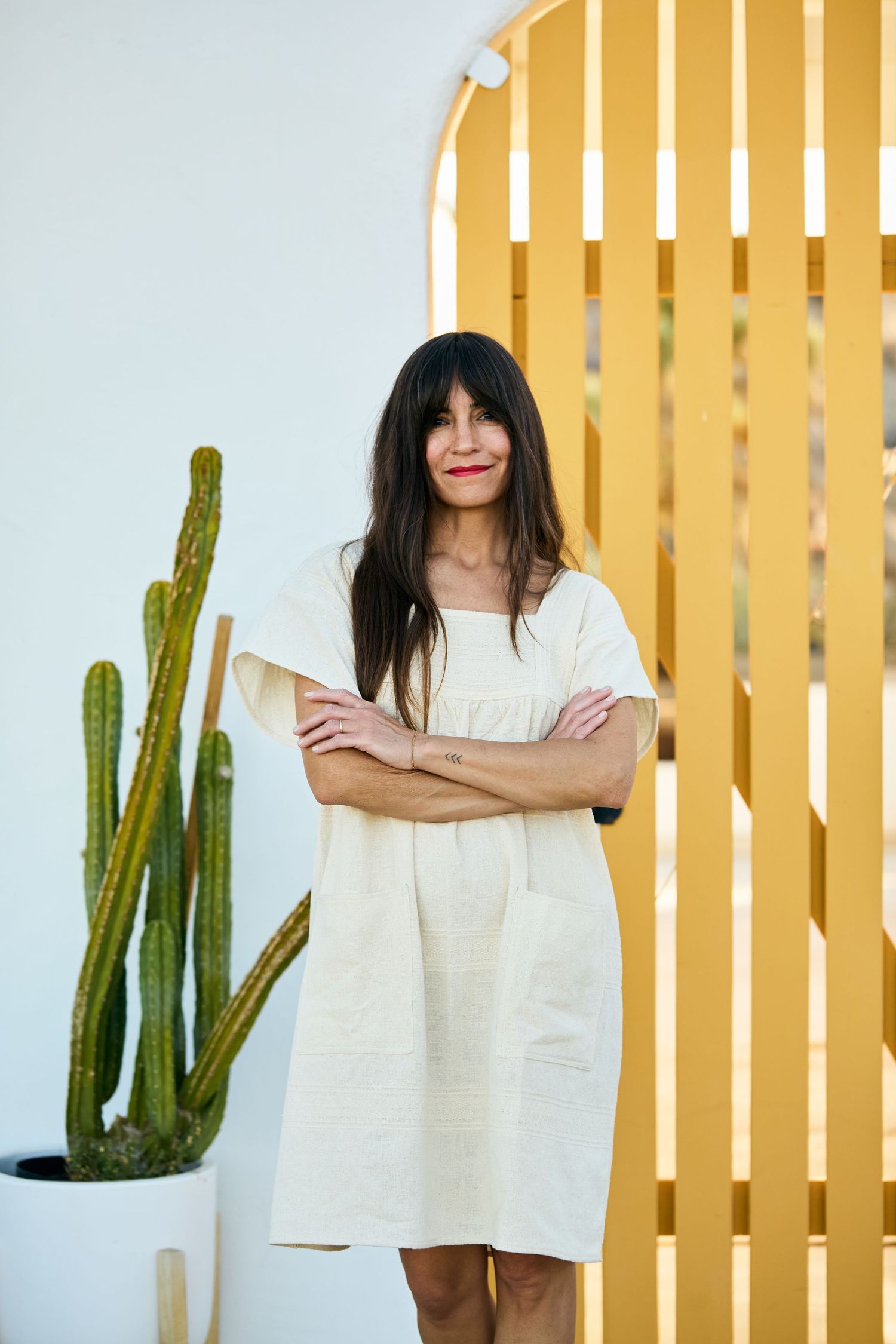 A person in a white dress stands against a yellow striped wall with tall cactus plants in multiple similar poses.