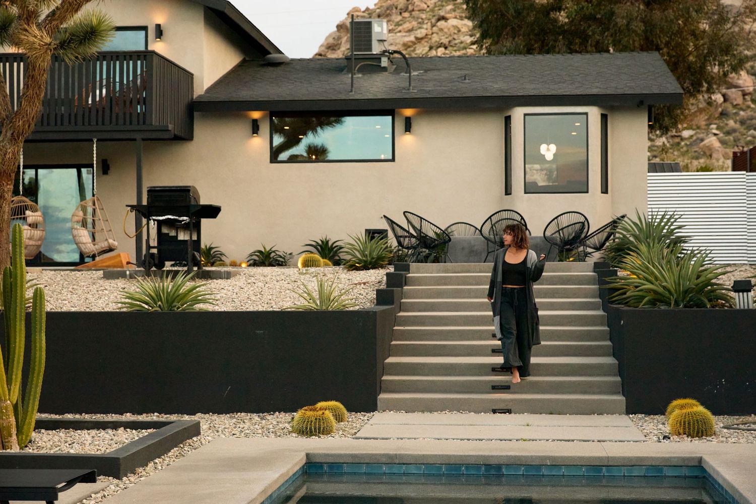 Woman walking up desert landscaped steps beside a pool at a modern Joshua Tree home with mountain views.