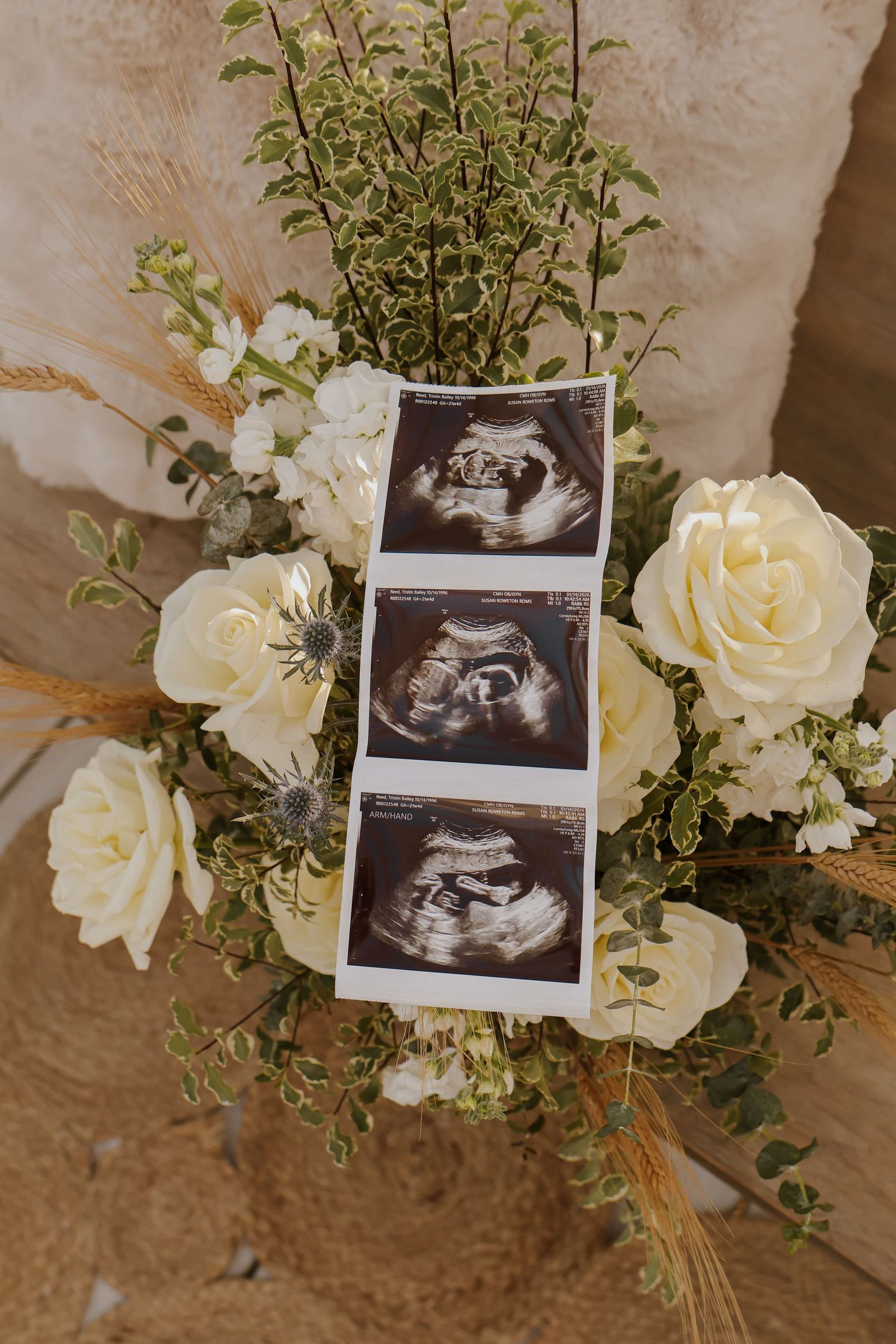 Ultrasound photos displayed with white roses and greenery in a romantic arrangement.