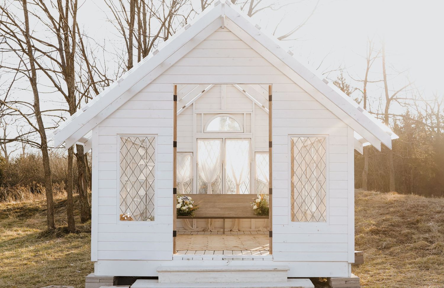 White wooden greenhouse exterior photographed at sunset.