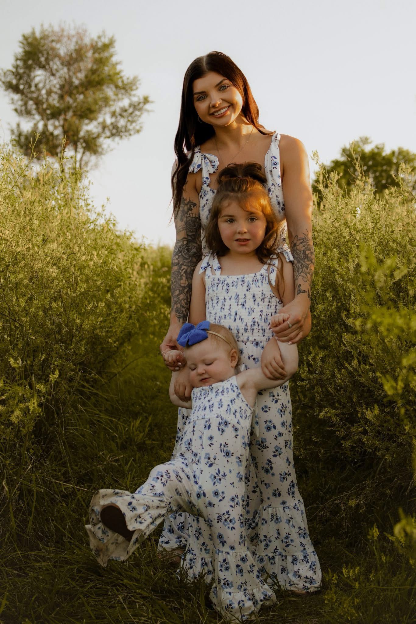 Family wearing matching floral dresses poses together in a field during golden hour.