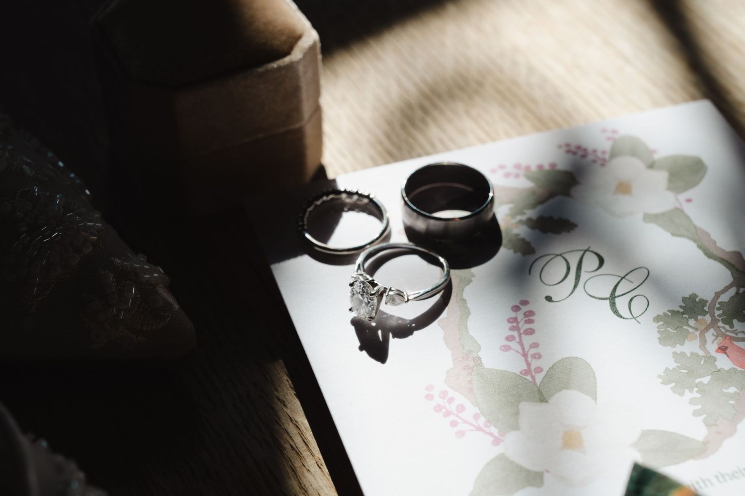 Three elegant wedding rings resting on a floral card, featuring a diamond engagement ring and two wedding bands in soft natural light.