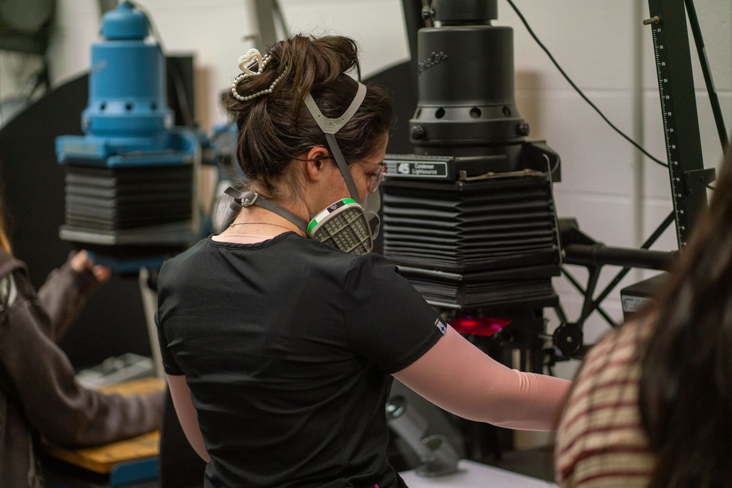 Woman wearing a respirator mask works on industrial equipment in a workshop setting.