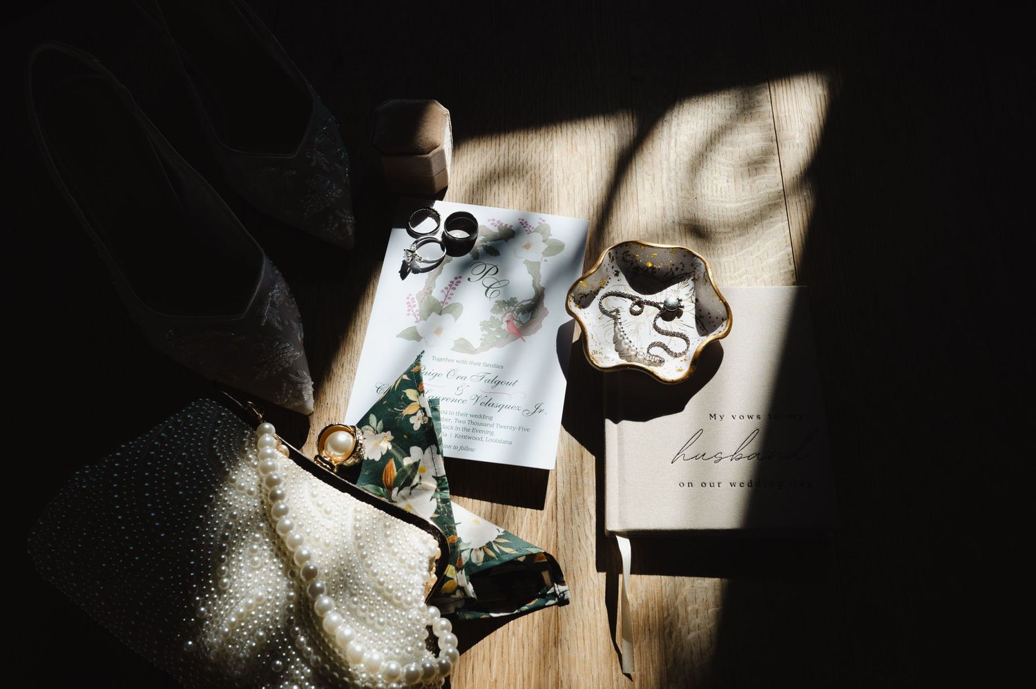 Wedding flat lay with invitation, rings, and accessories arranged on wooden surface with dramatic shadow light.