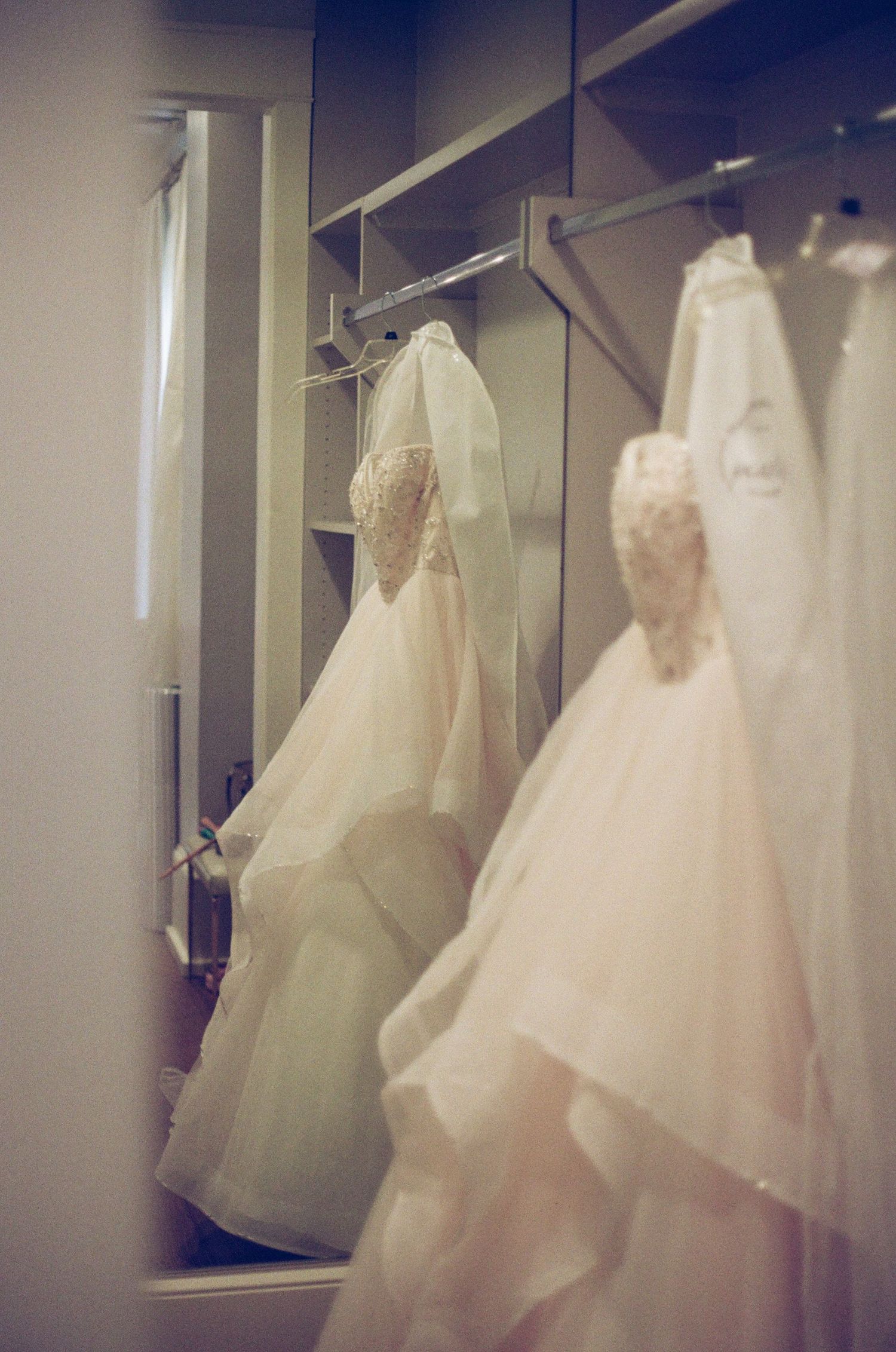 Wedding gowns with veils hang in a bridal boutique dressing room reflected in a mirror.