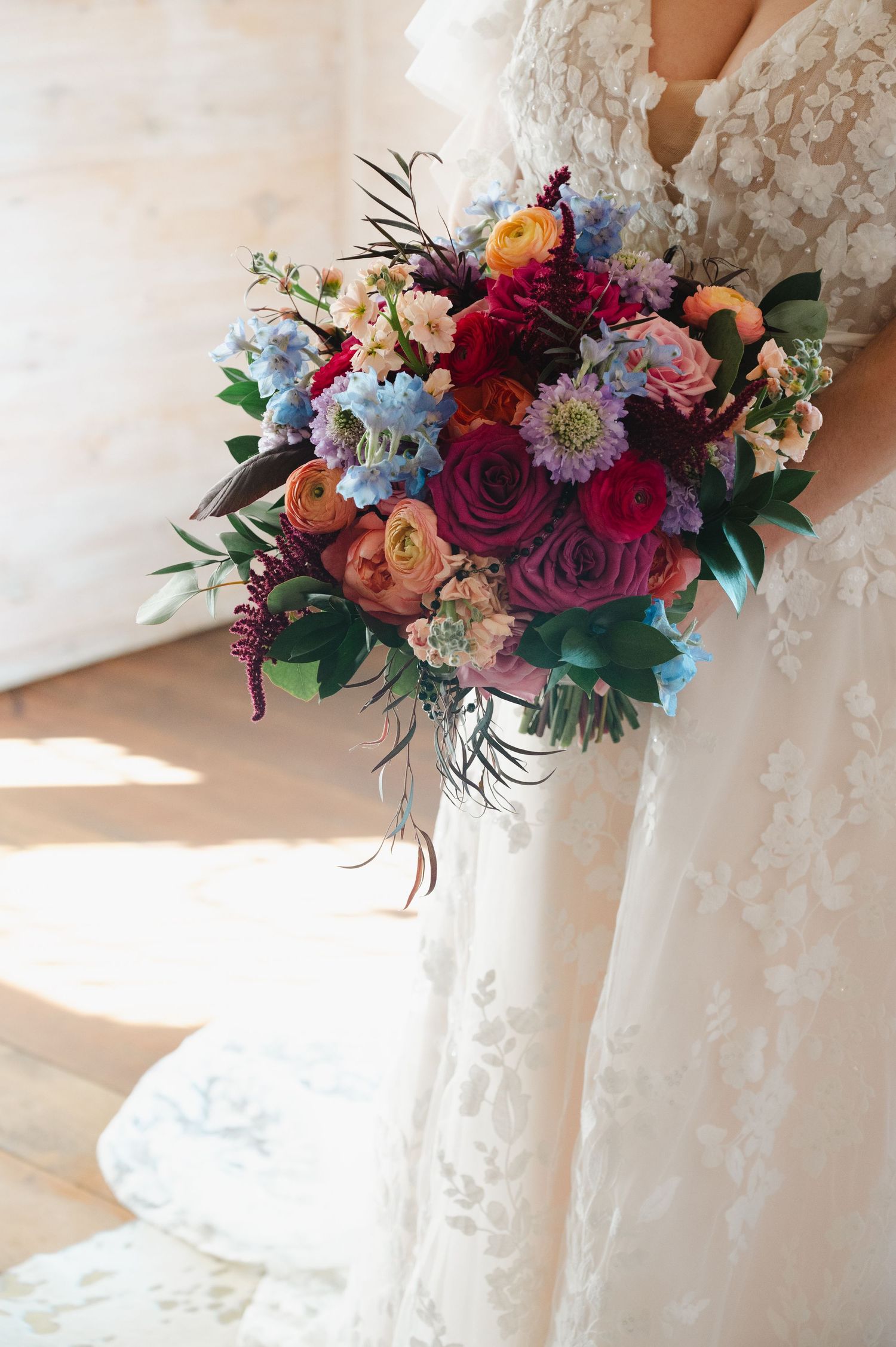 Bride in lace wedding gown holding a lush, colorful bridal bouquet with red, blue, and purple flowers.