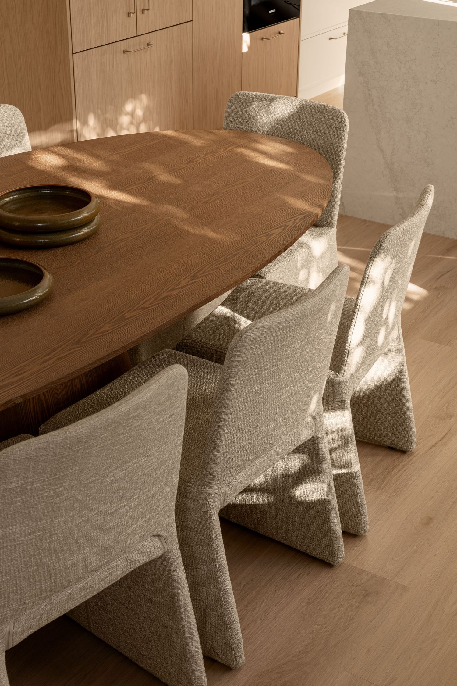 Modern dining room interior with wooden table and upholstered gray chairs in warm natural lighting.