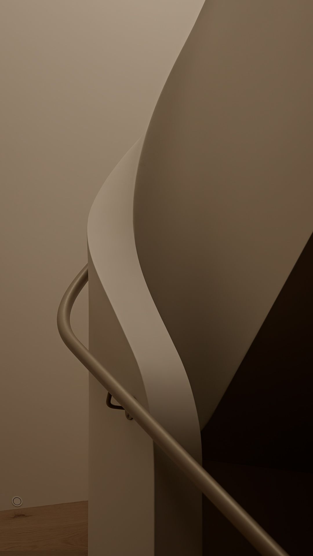 A curved staircase handrail follows the sweeping lines of a modern interior wall in sepia tones.