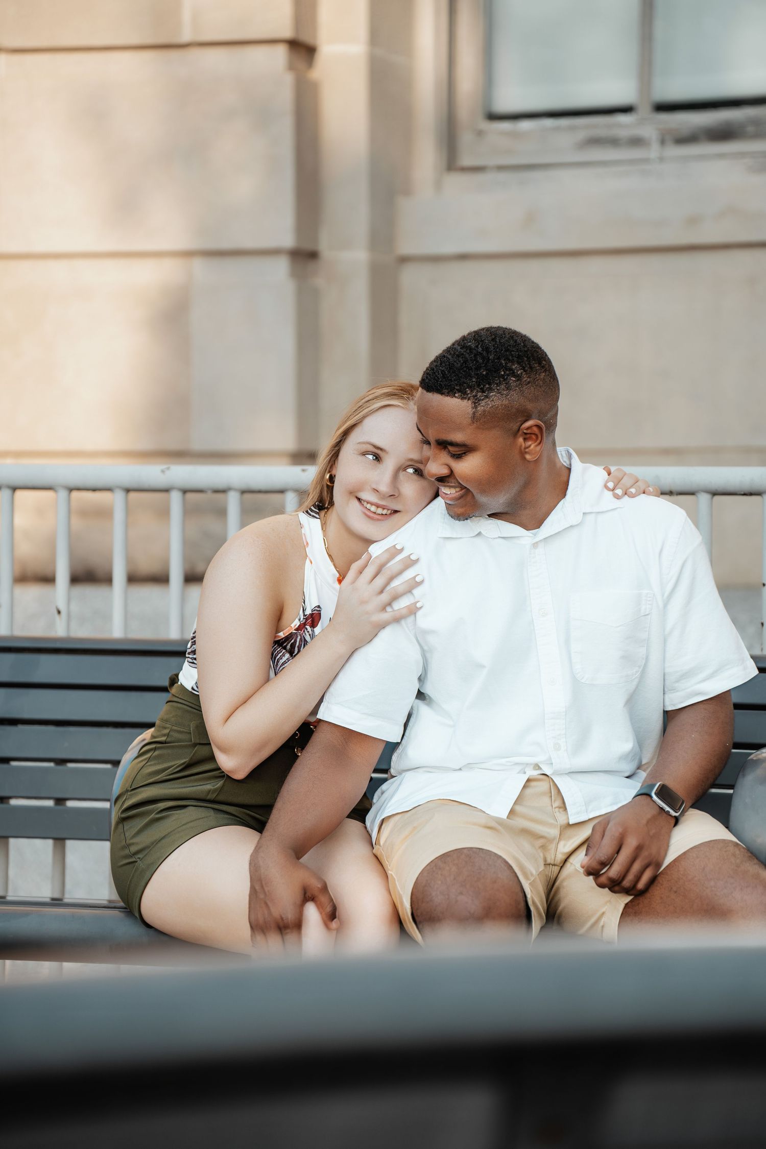 A couple shares an intimate moment while sitting together on a bench outside a building.