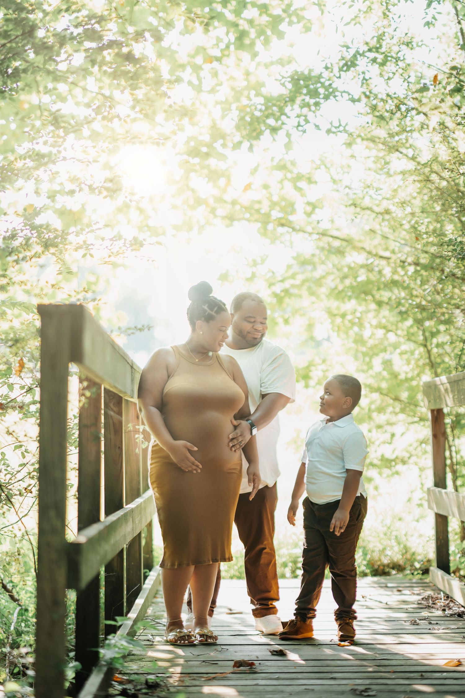 A family stands together on a wooden bridge walkway in a sun-drenched forest setting during a bright afternoon.