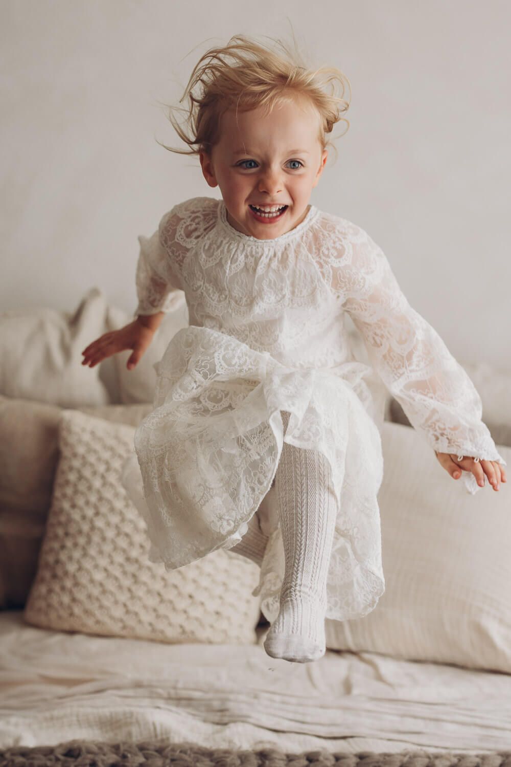 Fröhliches Mädchen springt lachend auf einem Bett im hellen Fotostudio – authentische Kinderfotografie in Hannover und Barsinghausen