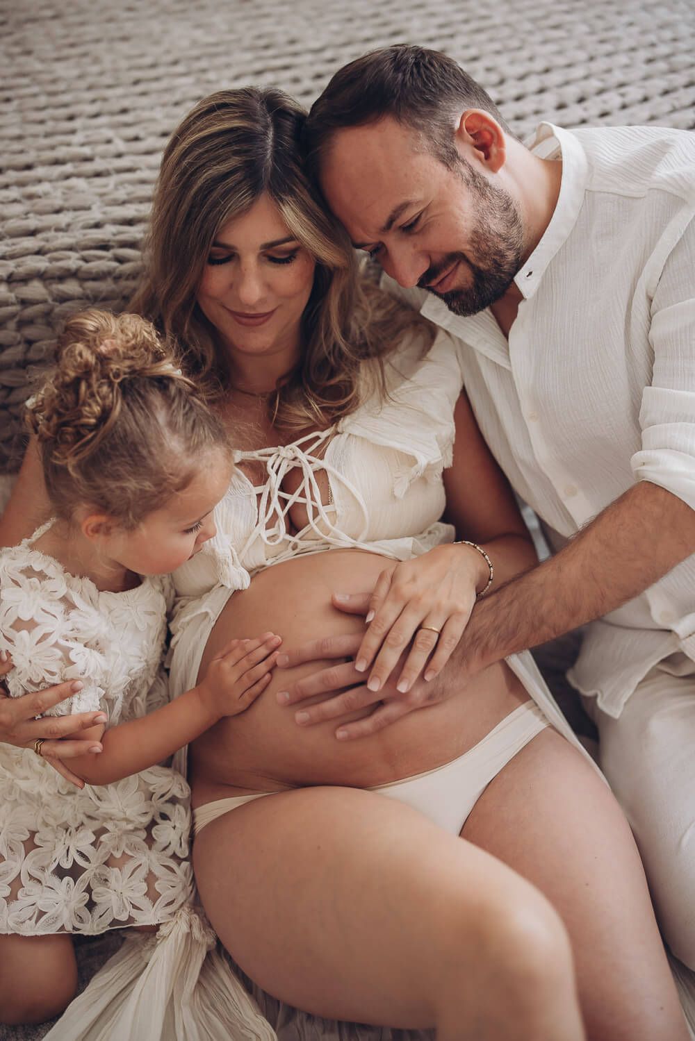 Familiäres Babybauch Fotoshooting in Hannover – Eltern und Kind sitzen zusammen auf dem Sofa und berühren den Babybauch