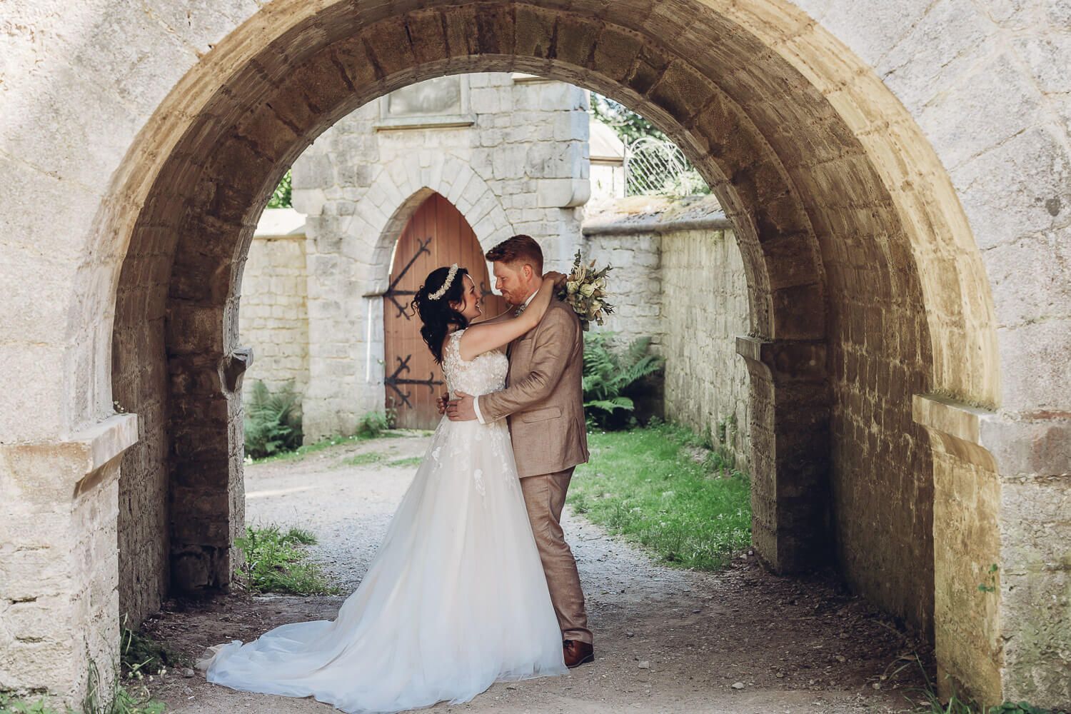 Brautpaar umarmt sich unter einem historischen Steinbogen bei seinem Hochzeitsshooting an der Schloss Marienburg
