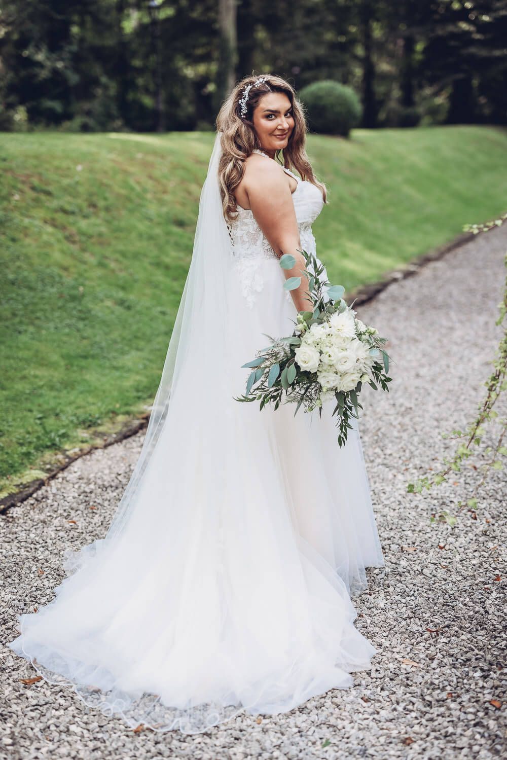 Brautportrait im Grünen mit langem Schleier und locker gehaltenem Brautstrauß, fotografiert von einem Hochzeitsfotografen in Minden