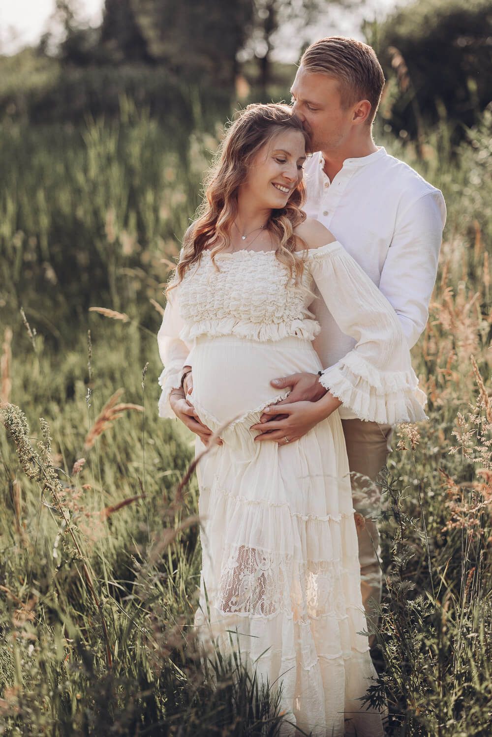 Paar umarmt sich liebevoll im hohen Gras während eines Babybauchshootings im Sonnenlicht - Fotoshooting in Hildesheim