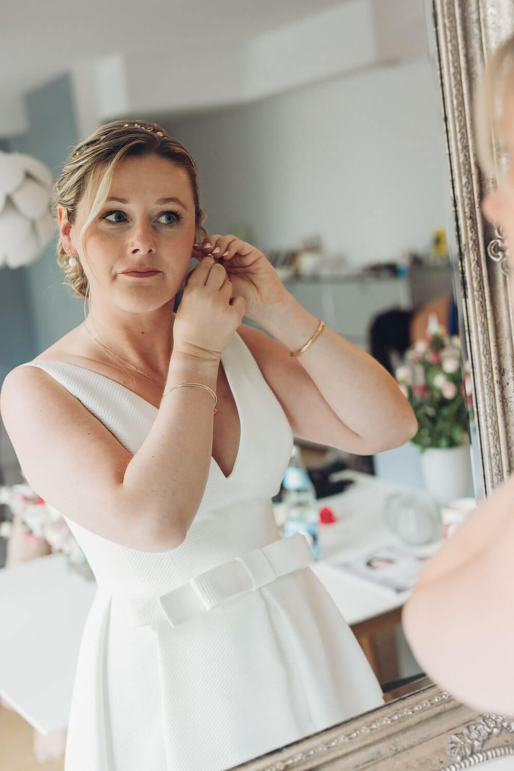 Braut steckt sich Ohrringe vor dem Spiegel beim Getting Ready für die Hochzeit in Hannover begleitet von einer Fotografin